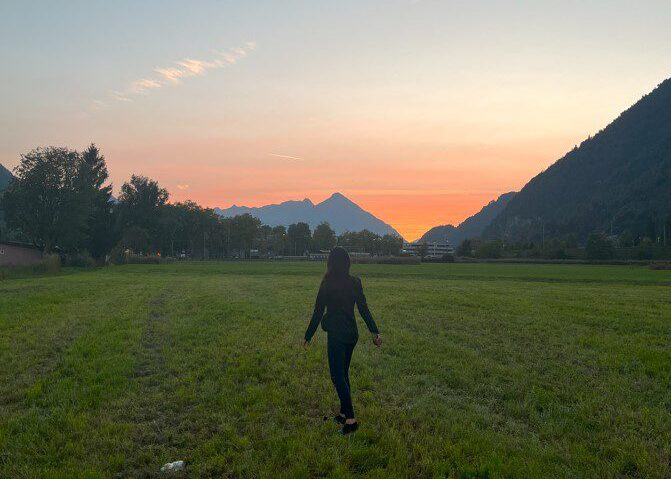 Alviya Siddiqui walking on grass. Mountain and sunset in background