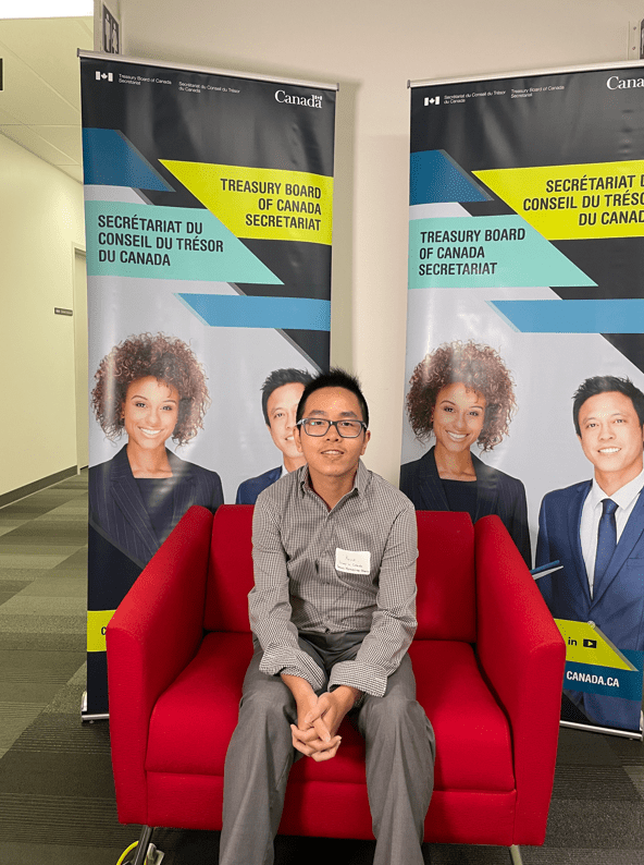 Kevin Nguyen sitting on red chair in front of Treasury Board of Canada banners